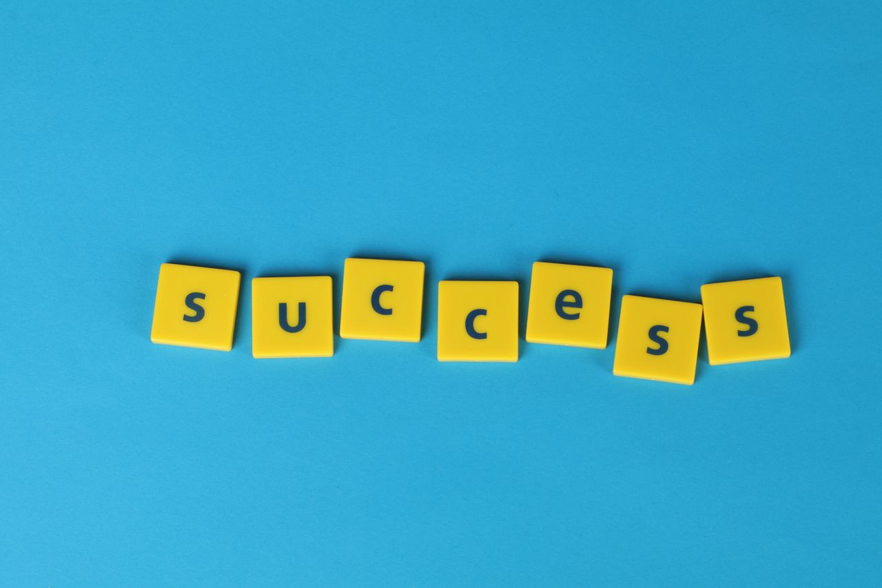 About Yellow letter tiles spell the word success on a vibrant blue backdrop, symbolizing achievement.